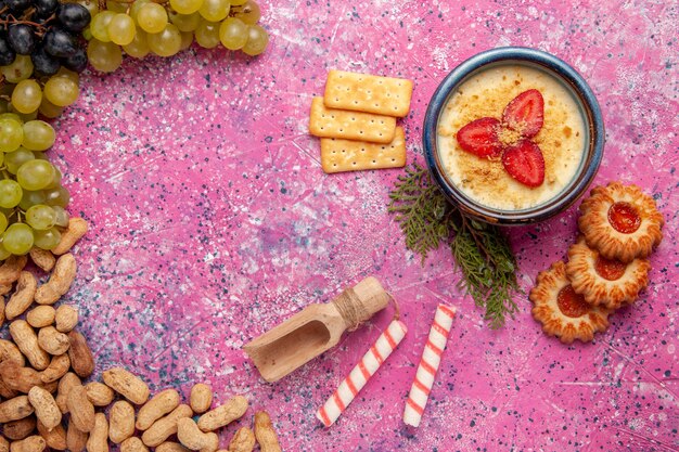 Bovenaanzicht heerlijk romig dessert met verse druiven, koekjes, crackers en pinda's op lichtroze bureau dessertijs bessen room zoet fruit