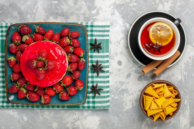 Bovenaanzicht heerlijke aardbeientaart beetje met verse aardbeien en kopje thee op lichtwitte ondergrond cake koekje bessen suiker zoet koekje