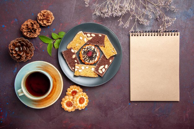 Bovenaanzicht heerlijke cake plakjes met koekjes en kopje thee op donkere achtergrond biscuit cookie cake thee zoet dessert