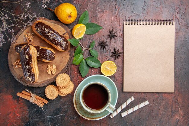 Bovenaanzicht heerlijke choco eclairs met kopje thee op donkere tafel dessertsnoepjes cake