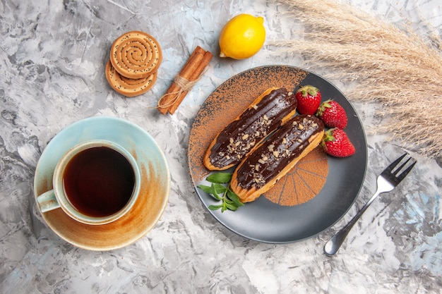 Bovenaanzicht heerlijke choco eclairs met kopje thee op lichte tafel dessert koekjes cake