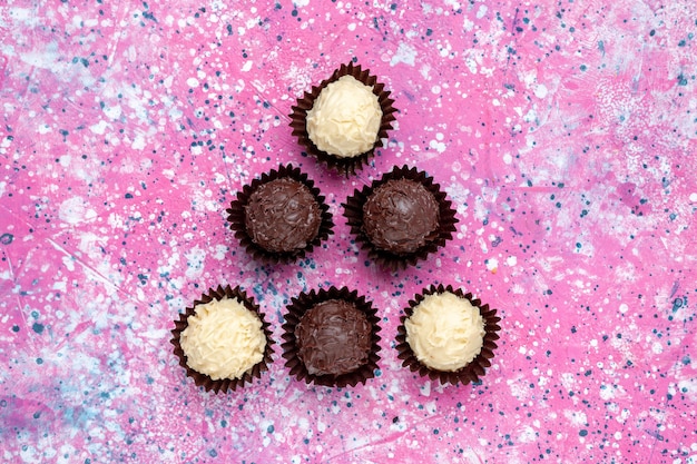 Bovenaanzicht heerlijke chocolade snoepjes witte en donkere chocolade op roze achtergrond.