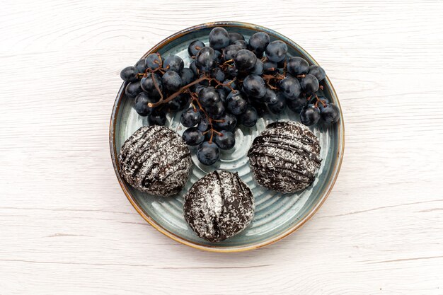 Bovenaanzicht heerlijke chocoladetaart met zwarte druiven op witte achtergrond cakekoekje zoete suiker taart fruit