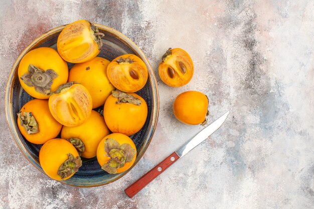 Bovenaanzicht heerlijke dadelpruimen in een kom persimmon en mes op naakte achtergrond