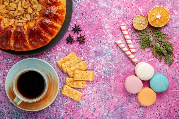 Bovenaanzicht heerlijke gebakjecake met rozijnen thee macarons crackers op roze bureau
