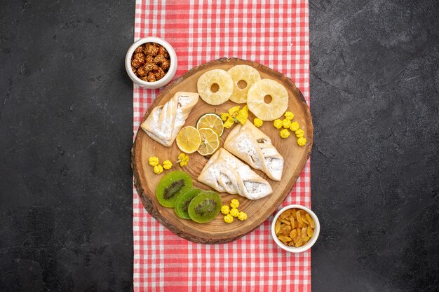 Bovenaanzicht heerlijke gebakjes met gedroogde ananasringen en kiwi's op grijze ruimte