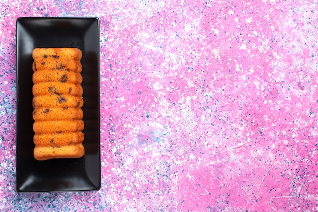 Bovenaanzicht heerlijke gebakken cake in zwarte cakevorm op het roze bureau.