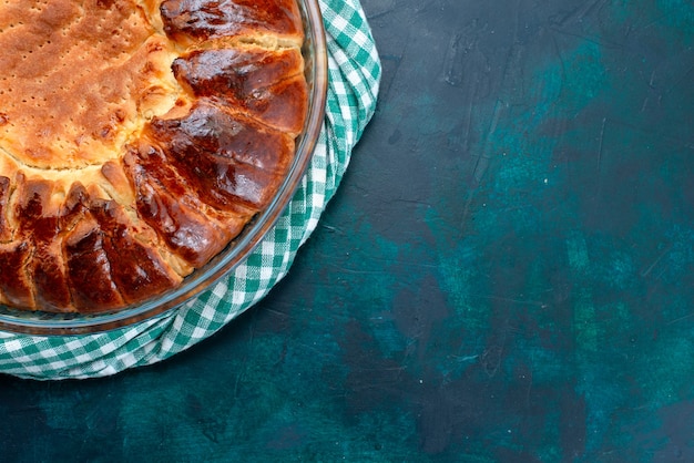 Bovenaanzicht heerlijke gebakken cake ronde gevormd zoet binnen glazen pan op lichtblauwe achtergrond.