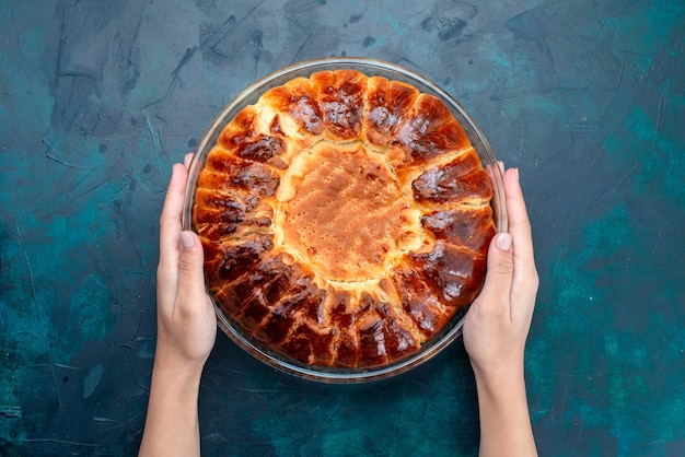 Bovenaanzicht heerlijke gebakken cake ronde gevormde zoete binnen glazen pan op de lichtblauwe achtergrond.