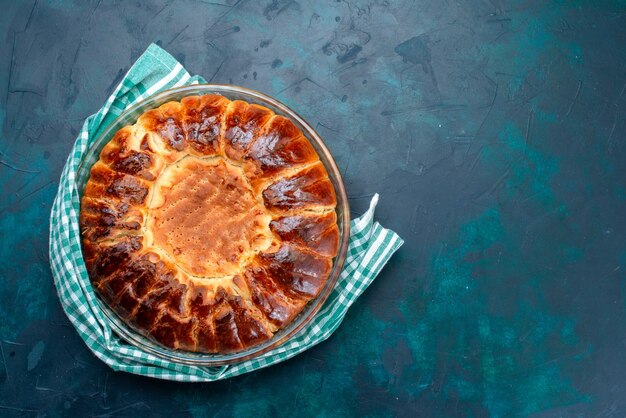 Bovenaanzicht heerlijke gebakken cake ronde gevormde zoete binnenkant glazen pan op lichtblauwe vloer.