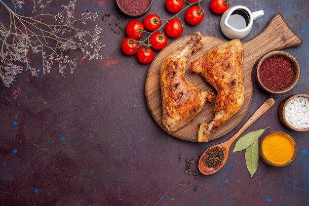 Bovenaanzicht heerlijke gebakken kip met kruiden en groenten op donker bureau