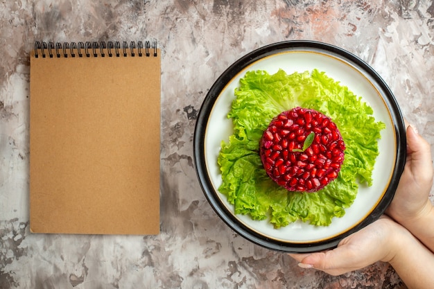 Bovenaanzicht heerlijke granaatappelsalade rond gevormd op groene salade met notitieblok op de lichte achtergrond