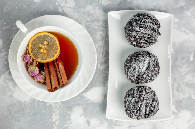 Bovenaanzicht heerlijke kleine cakes met poedersuiker kaneel en kopje thee op witte ondergrond thee biscuit cake bakken suiker zoete taart