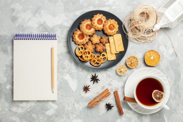 Bovenaanzicht heerlijke koekjes met crackers en chips binnen plaat met kopje thee op het licht witte bureau koekje koekje suiker zoete thee chips