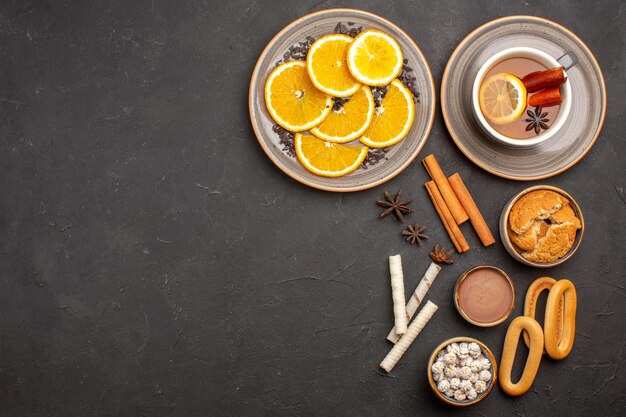 Bovenaanzicht heerlijke koekjes met gesneden sinaasappels en kopje thee op donkere achtergrond suikerkoekje fruit zoet koekje