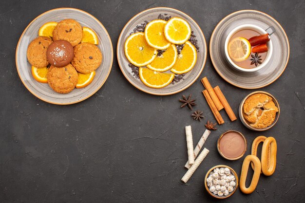 Bovenaanzicht heerlijke koekjes met gesneden sinaasappels en kopje thee op donkere achtergrond suikerkoekje fruit zoet koekje