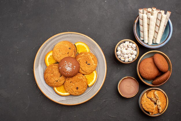 Bovenaanzicht heerlijke koekjes met pijpkoekjes en sinaasappels op donkere oppervlakte fruitkoekje dessert citruskoekje zoet