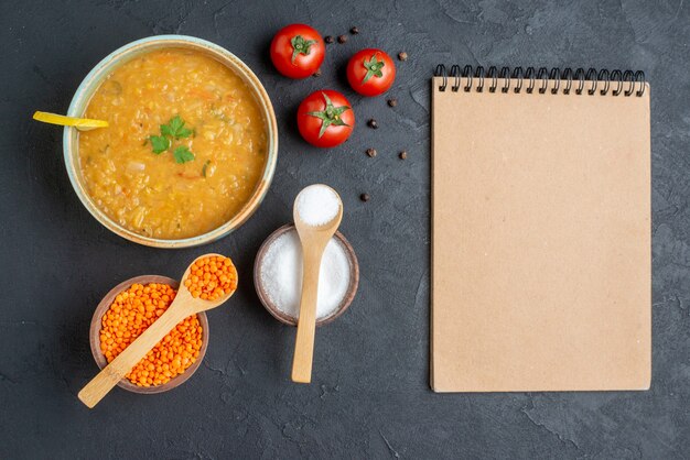 Bovenaanzicht heerlijke linzensoep met zout en rode tomaten op donkere ondergrond
