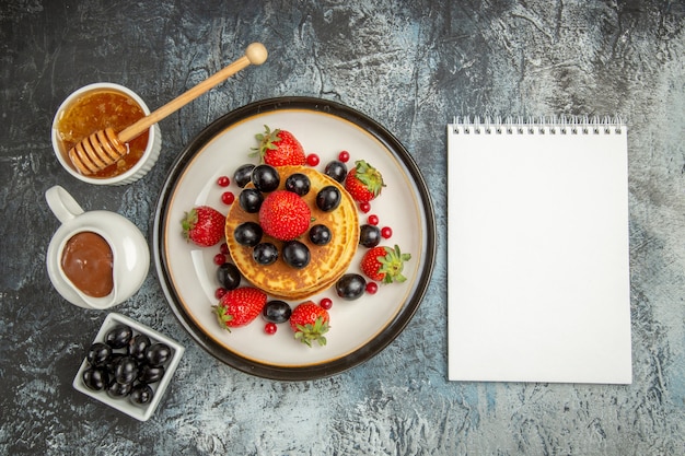 Bovenaanzicht heerlijke pannenkoeken met honing en fruit op lichte zoete fruitcake