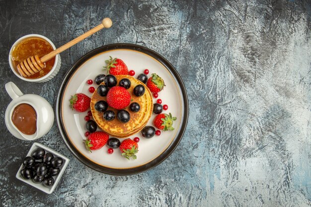 Bovenaanzicht heerlijke pannenkoeken met honing en fruit op lichte zoete fruitcake