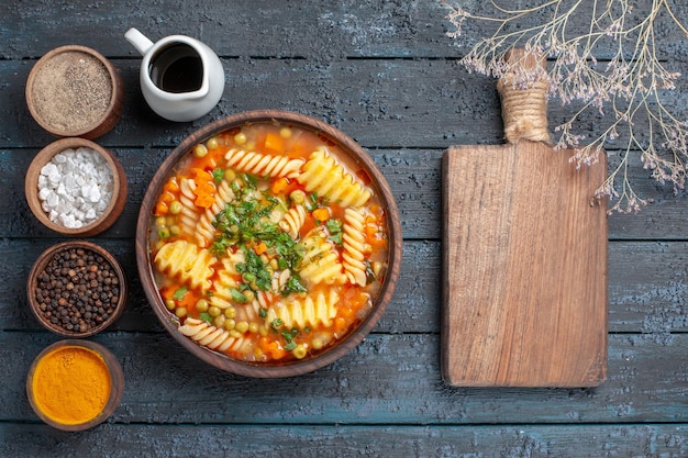 Bovenaanzicht heerlijke pastasoep van spiraalpasta met smaakmakers op de donkerblauwe bureausaus keukenschotel italiaanse pastasoep