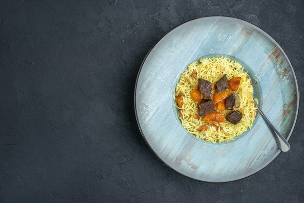 Bovenaanzicht heerlijke pilaf gekookte rijst met gedroogde abrikozen en vleesplakken binnen plaat op donkere ondergrond