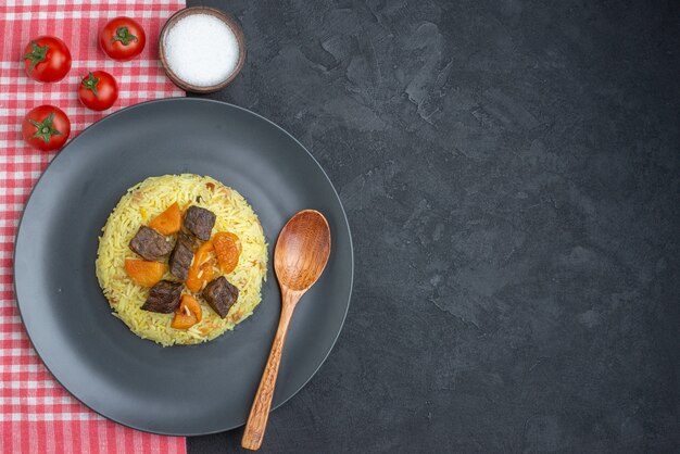 Bovenaanzicht heerlijke pilaf gekookte rijst met vlees plakjes zout en tomaten op donkere ondergrond