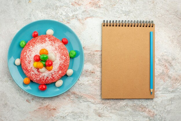 Bovenaanzicht heerlijke roze cake met kleurrijke snoepjes in plaat op wit oppervlak regenboog kleur taart taart dessert snoep