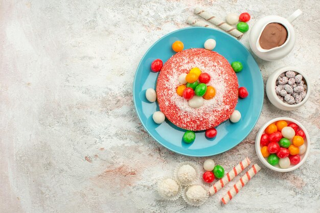 Bovenaanzicht heerlijke roze cake met kleurrijke snoepjes op witte oppervlakte dessert kleur goodie regenboog cake snoep