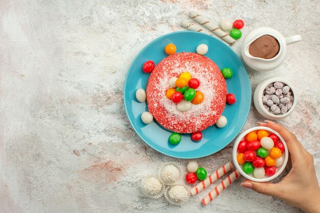 Bovenaanzicht heerlijke roze cake met kleurrijke snoepjes op witte oppervlakte dessert kleur regenboog snoep cake goodie