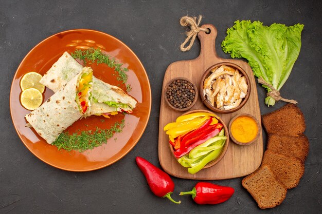 Bovenaanzicht heerlijke shaurma gesneden vleessandwich met donker brood en groenten op donkere achtergrond snackvoedsel sandwich hamburger