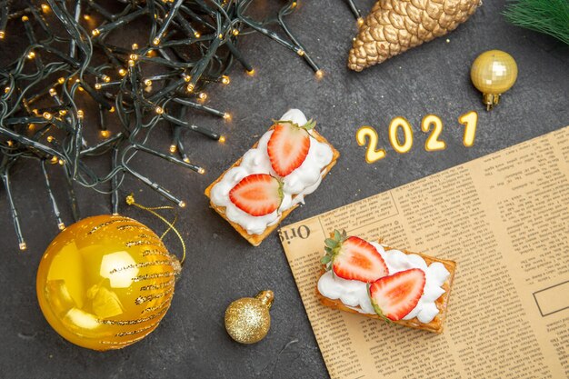 Bovenaanzicht heerlijke slagroomtaarten met aardbeien rond nieuwjaarsboomspeelgoed op donkere achtergrond