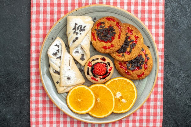 Bovenaanzicht heerlijke suikerkoekjes met gebak en sinaasappel op donkere oppervlakte cake suikerkoekje zoete koekjes thee