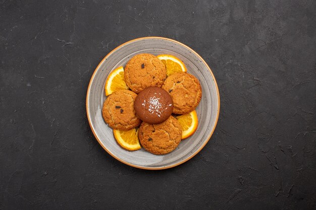 Bovenaanzicht heerlijke suikerkoekjes met gesneden sinaasappels in een bord op een donkere achtergrond, suikerfruitkoekje, zoet koekje