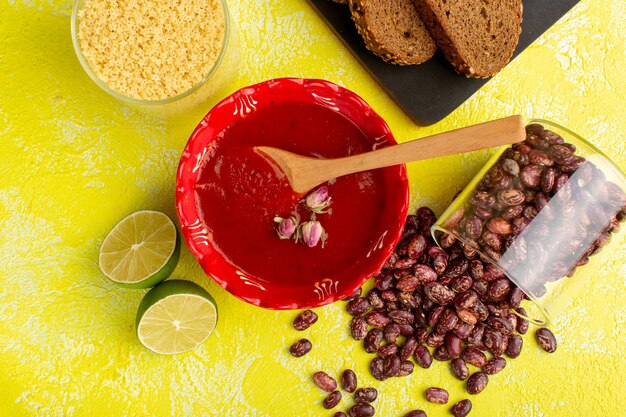 Bovenaanzicht heerlijke tomatensaus met donkere broodbroodjes citroen en rauwe bonen op geel bureau soep eten maaltijd diner