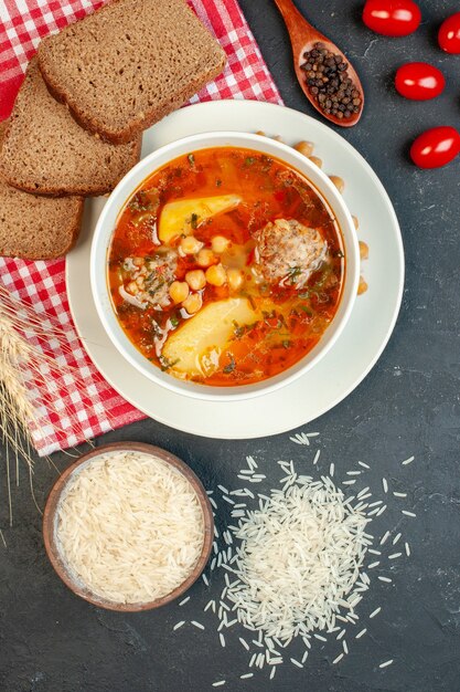 Bovenaanzicht heerlijke vleessoep met brood en tomaten op de donkere achtergrond