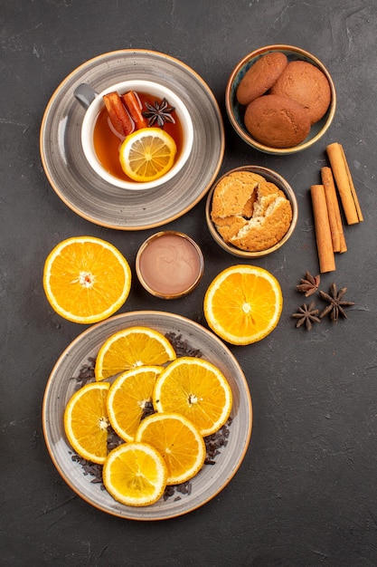 Bovenaanzicht heerlijke zandkoekjes met vers gesneden sinaasappels en kopje thee op donkere achtergrond, suikerkoekje, zoet koekjesfruit