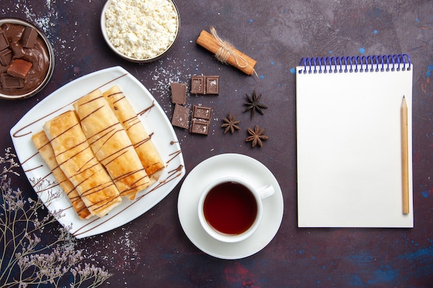 Bovenaanzicht heerlijke zoete gebakjes met chocolade en kopje thee op donkere vloer bakken dessert suiker koektaart zoet