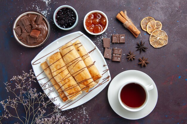 Bovenaanzicht heerlijke zoete gebakjes met chocoladejam en kopje thee op donkere ruimte