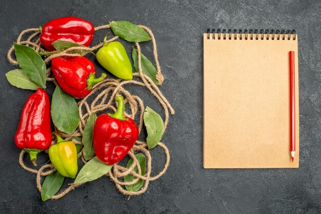 Bovenaanzicht heldere paprika's met laurierblaadjes naast notebook rode pen op grijze achtergrond met vrije ruimte