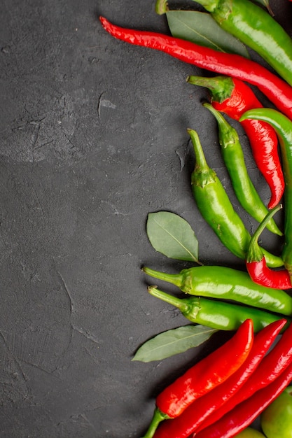 Bovenaanzicht hete rode en groene paprika's laurierblaadjes op zwarte grond met vrije ruimte