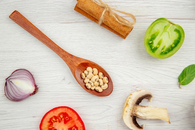 Bovenaanzicht houten lepel met bonen champignons groene tomaat ui kaneelstokjes op grijze tafel