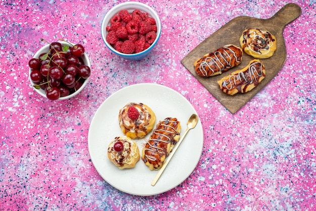 Bovenaanzicht in de verte heerlijke fruitige taarten met room en chocolade in witte plaat samen met vers fruit op de roze achtergrond cake koekje zoet bakken