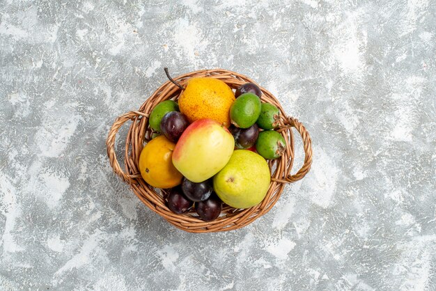 Bovenaanzicht in de verte plastic rieten mand met appelperen, feykhoas-pruimen en persimmon in het midden van de grijze tafel