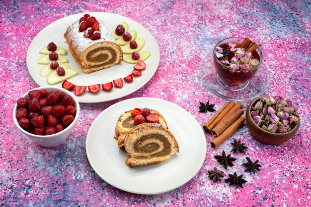 Bovenaanzicht in de verte roll cakeplakken met verschillende soorten fruit in witte plaat kaneelthee op het gekleurde bureau cake koekje zoet fruit