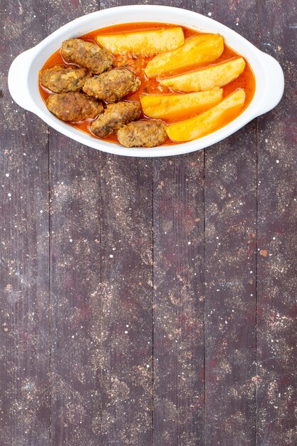 Bovenaanzicht in de verte smakelijke vleeskoteletten gekookt samen met aardappelen en saus in plaat op bruin, vlees aardappel gerecht maaltijd diner