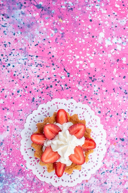 Bovenaanzicht in de verte van kleine romige cake met gesneden aardbeien op licht helder, cake biscuit bessen zoet bakken