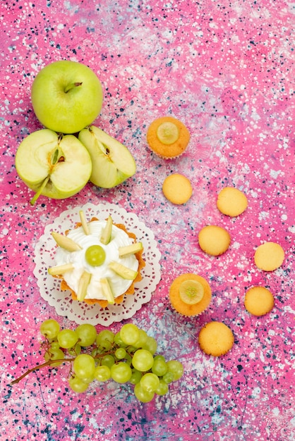 Bovenaanzicht in de verte van kleine romige cake met gesneden fruit op bureau, cake zoete suiker bakken