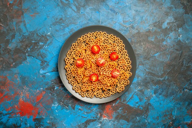 Bovenaanzicht Italiaanse pastaharten gesneden kerstomaatjes op zwarte ovale plaat op blauwe tafelkopieplaats