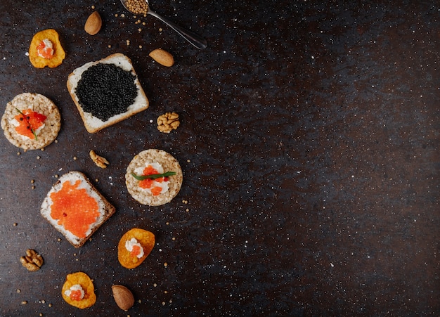 Bovenaanzicht kaviaar hapjes toast chips en knapperig knapperig brood met kwark rode kaviaar zwarte kaviaar tarhun amandel en walnoot aan de linkerkant met kopie ruimte op zwarte achtergrond